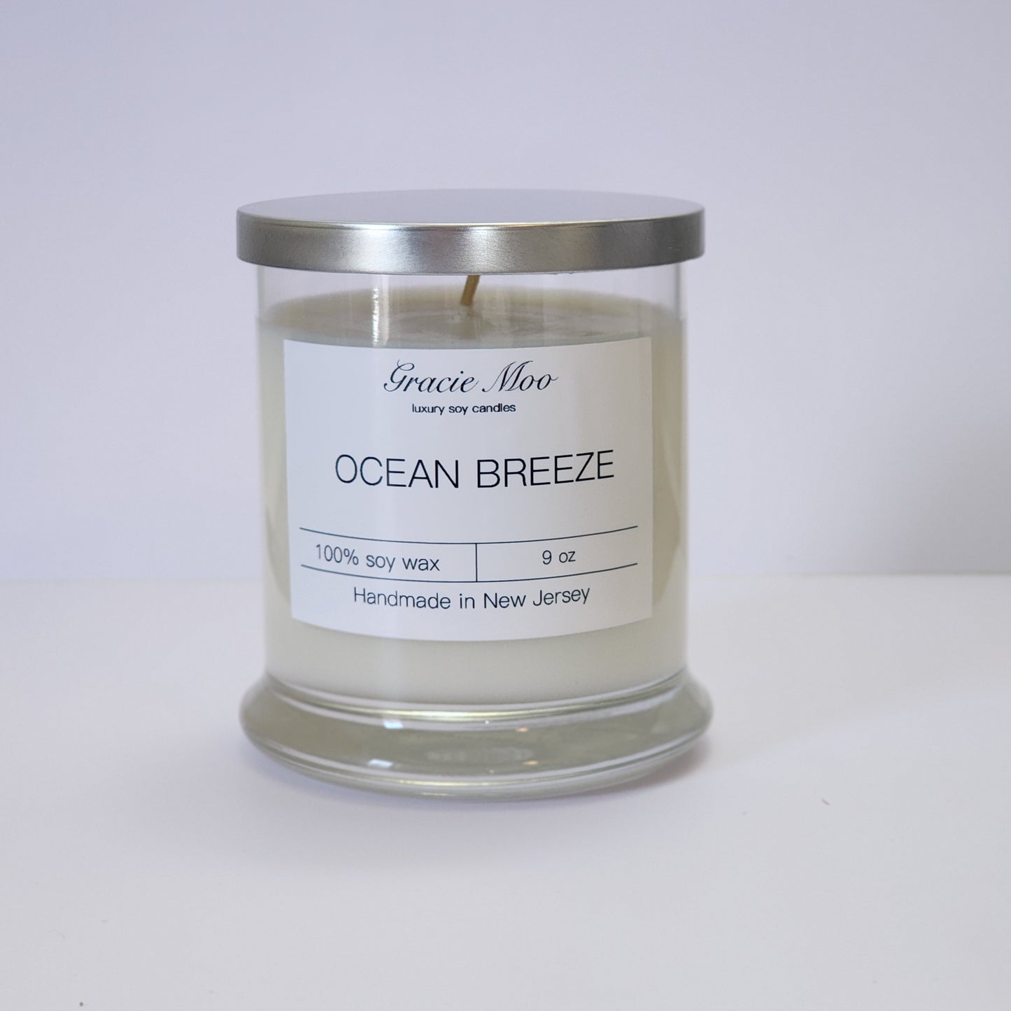 Ocean Breeze Status Candle by Gracie Moo Candles in a glass jar with a soft blue hue and a light, airy scent.