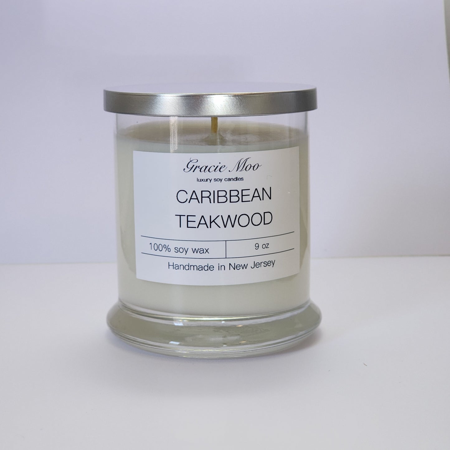 Gracie Moo Candles Caribbean Teakwood status candle with a warm, inviting glow and elegant glass container.