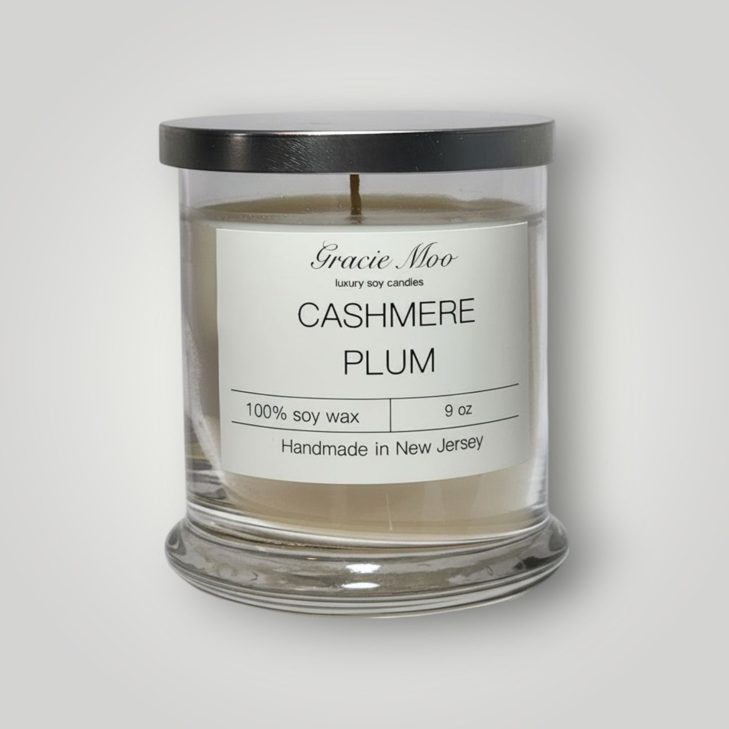 Gracie Moo Cashmere Plum Status Candle in a sleek glass container with a warm, inviting glow.