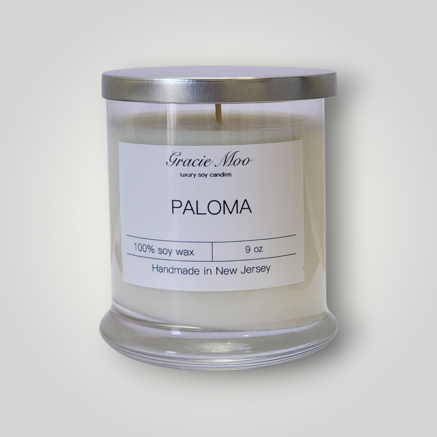 GracieMoo Paloma Status Candle in a stylish glass jar with a warm glow and intricate label design.