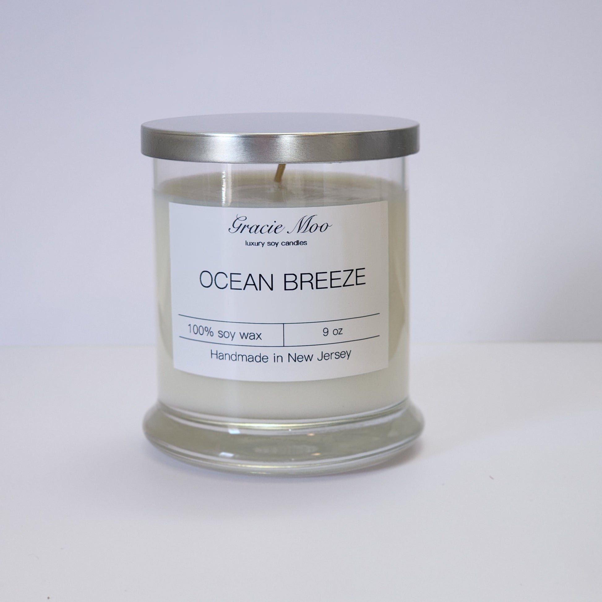 Ocean Breeze Status Candle by Gracie Moo Candles in a glass jar with a soft blue hue and a light, airy scent.
