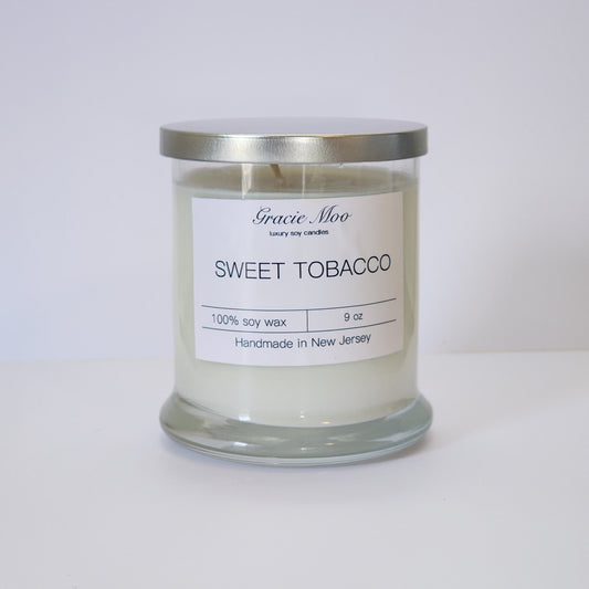 Sweet Tobacco Status Candle by Gracie Moo Candles, featuring a warm amber glow and rustic jar design.