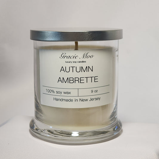Gracie Moo Candles Autumn Ambrette Status Candle in a stylish glass jar with warm autumn colors.