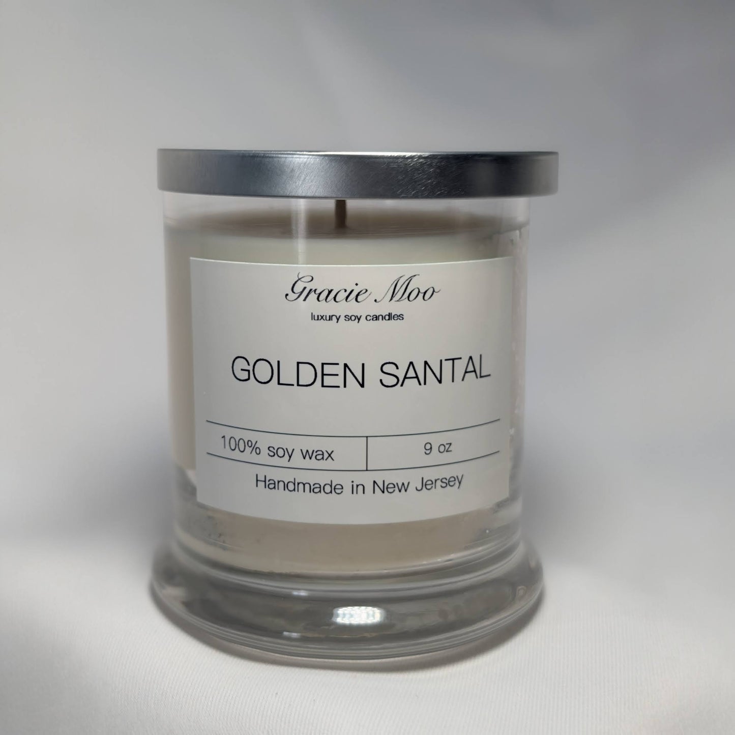 Golden Santal Status Candle by Gracie Moo Candles, featuring a sleek gold-colored container and a lit wicks aroma candle.
