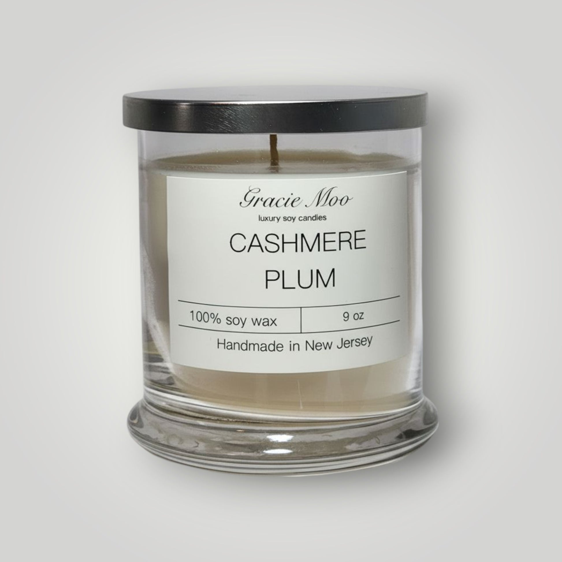 Gracie Moo Cashmere Plum Status Candle in a sleek glass container with a warm, inviting glow.