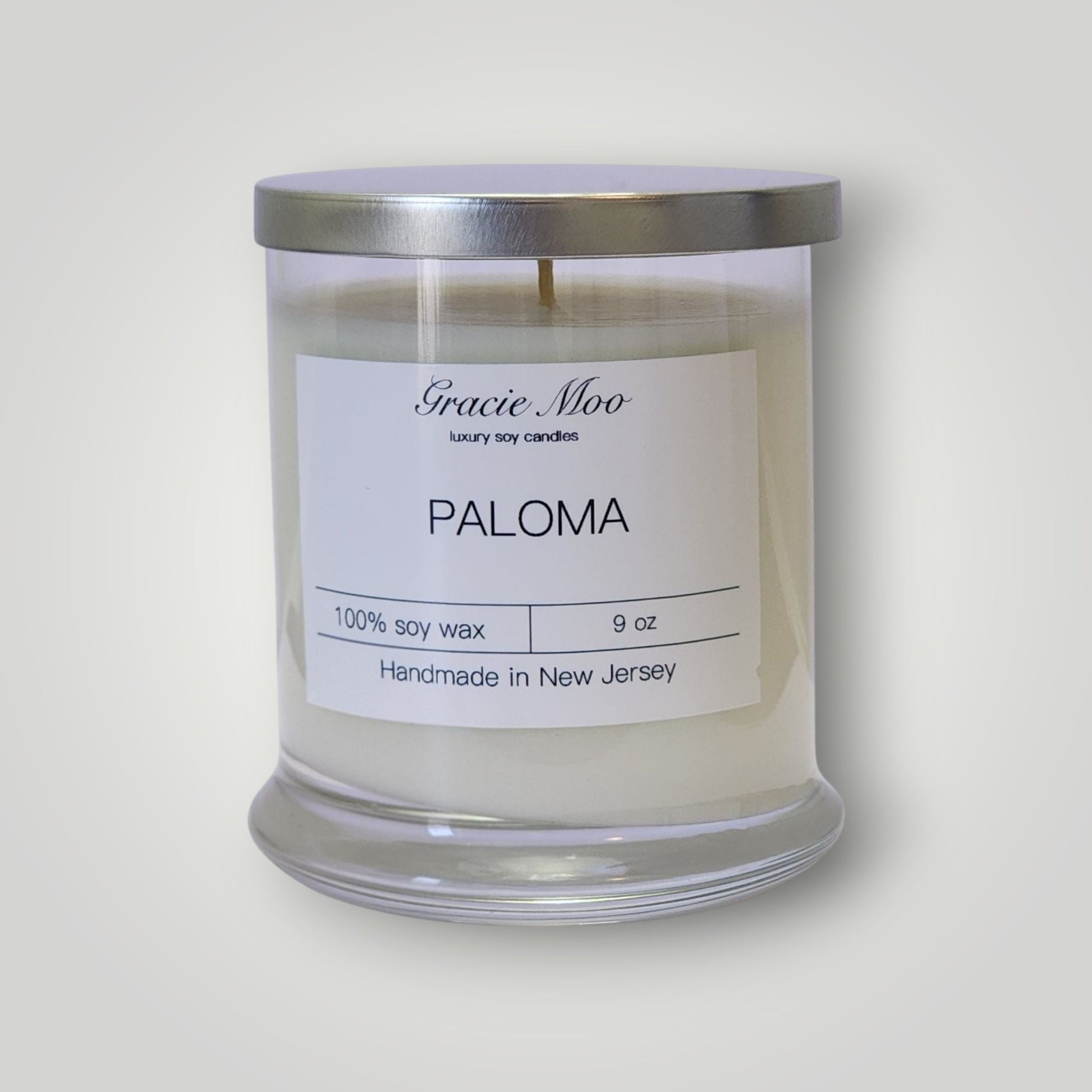 GracieMoo Paloma Status Candle in a stylish glass jar with a warm glow and intricate label design.